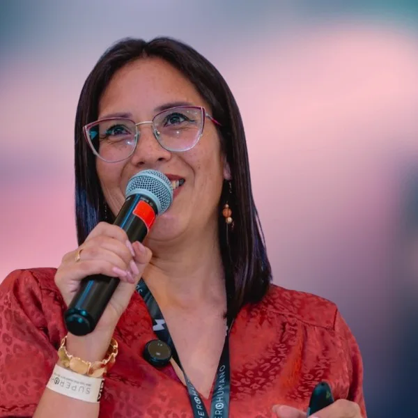 Reyna Ana habla con micrófono en un escenario, sonriendo.